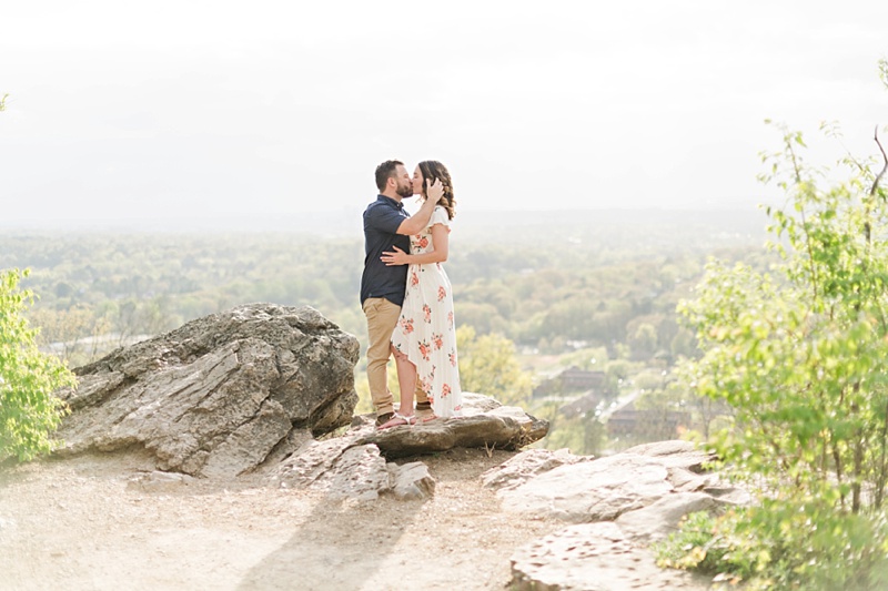 Spring engagement session on a cliff overlooking a city kissing.