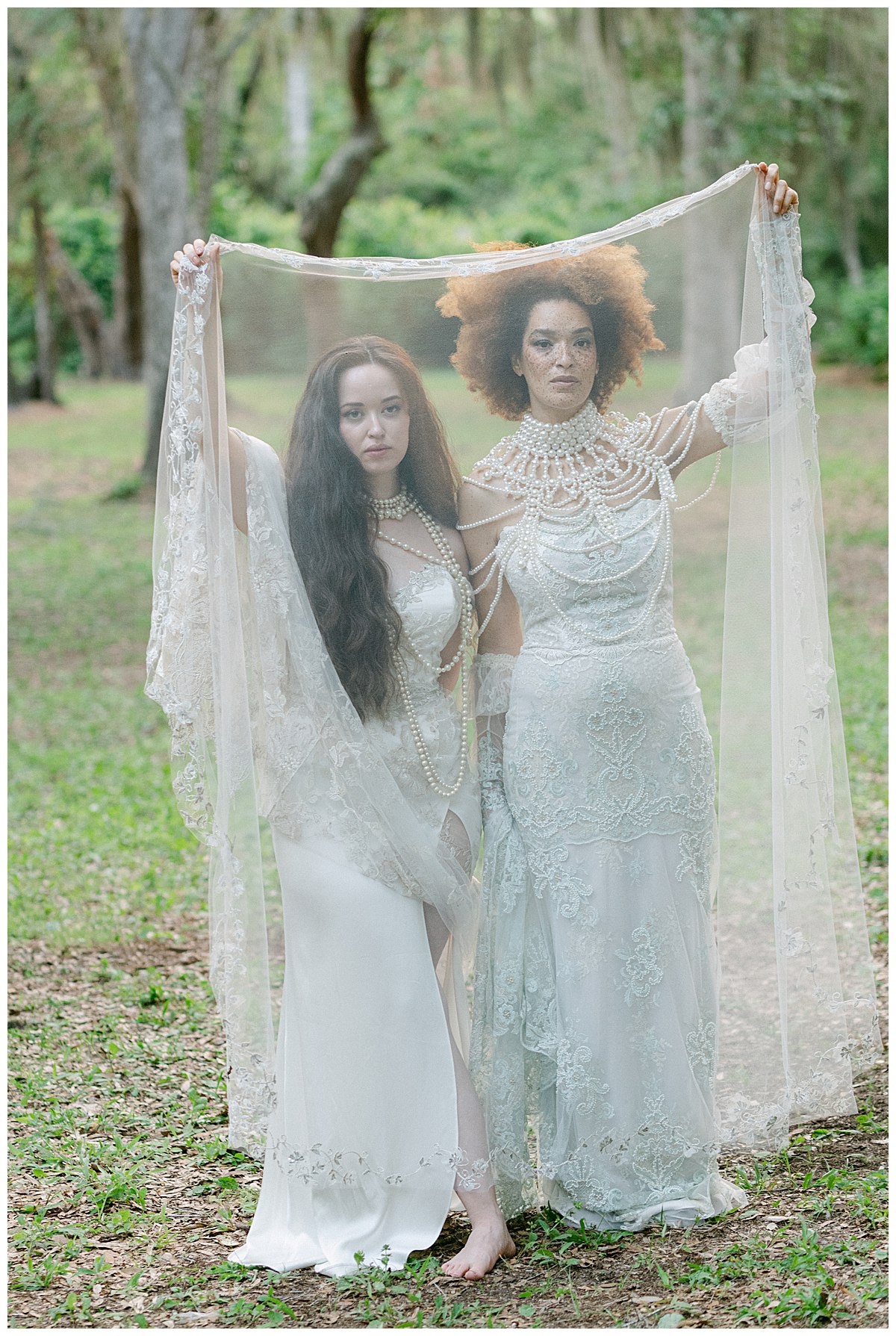 Two women models in white lace gowns looking through a lace veil